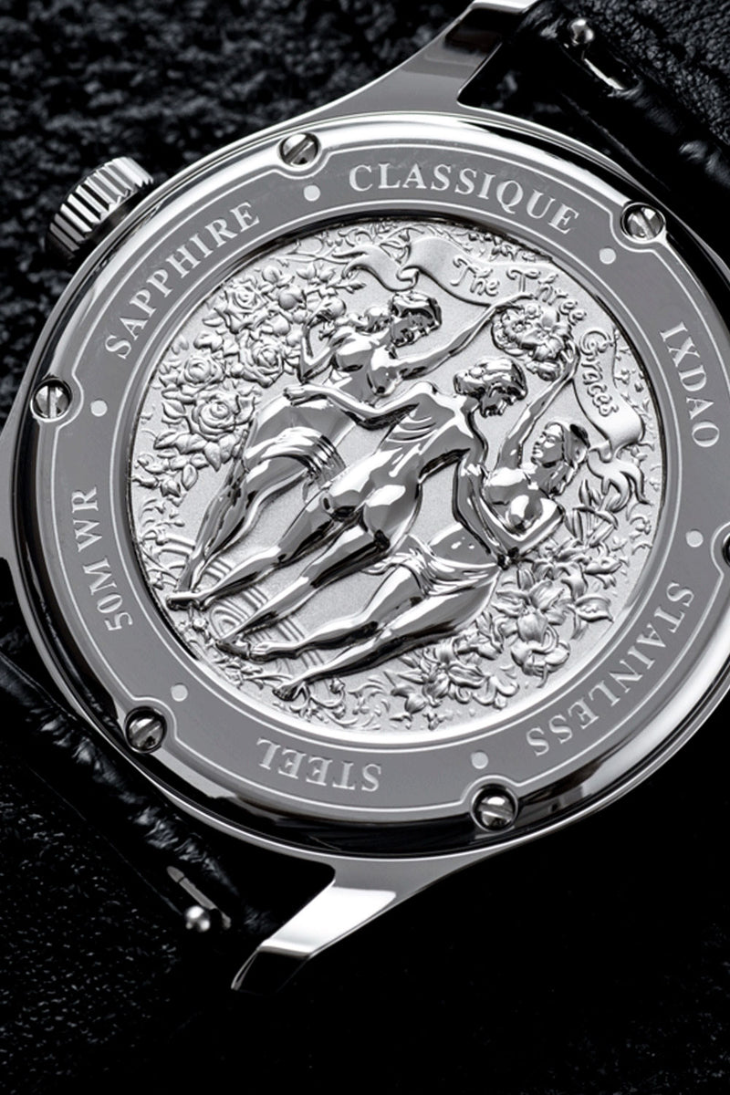 Close-up of the back of a stainless steel watch case with an ornate engraved figure design and text including 'SAPPHIRE', 'CLASSIQUE', 'STAINLESS', and '50 WR', set against a black leather strap on a dark textured background.