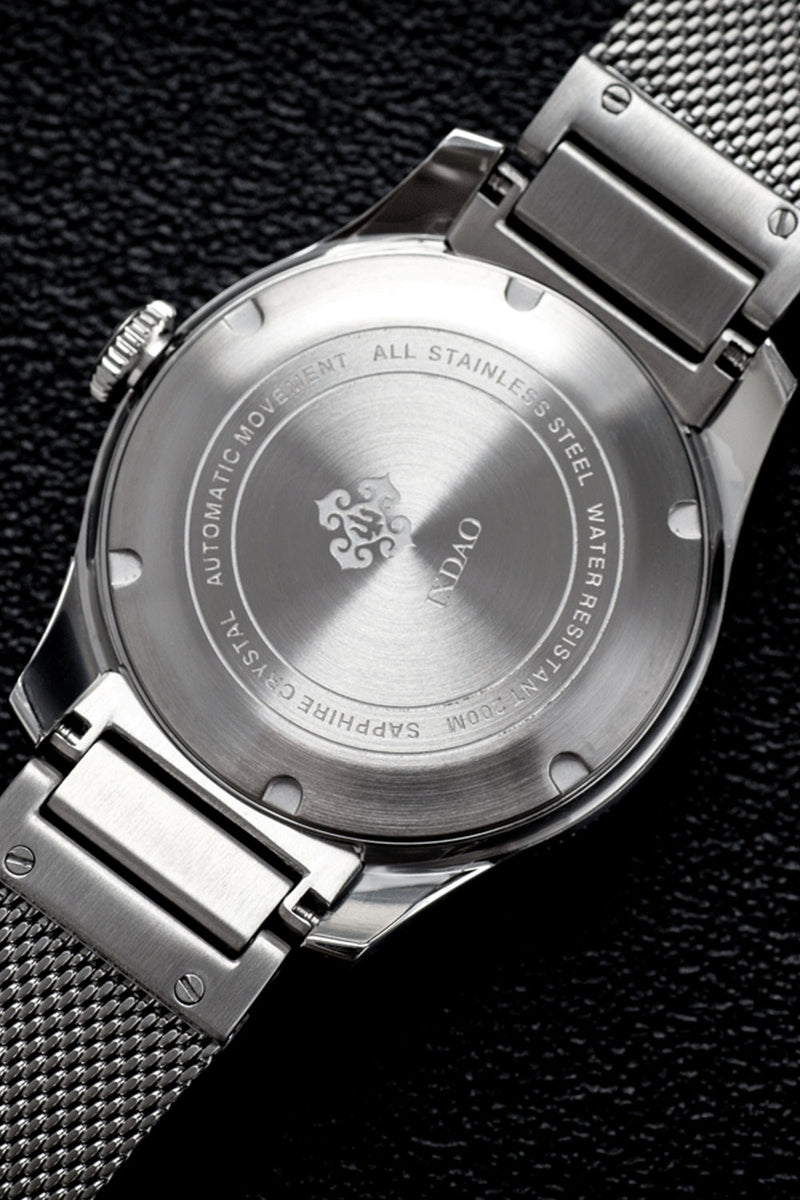 Close-up of the back case and metal mesh bracelet of a stainless steel wristwatch on a dark textured background.