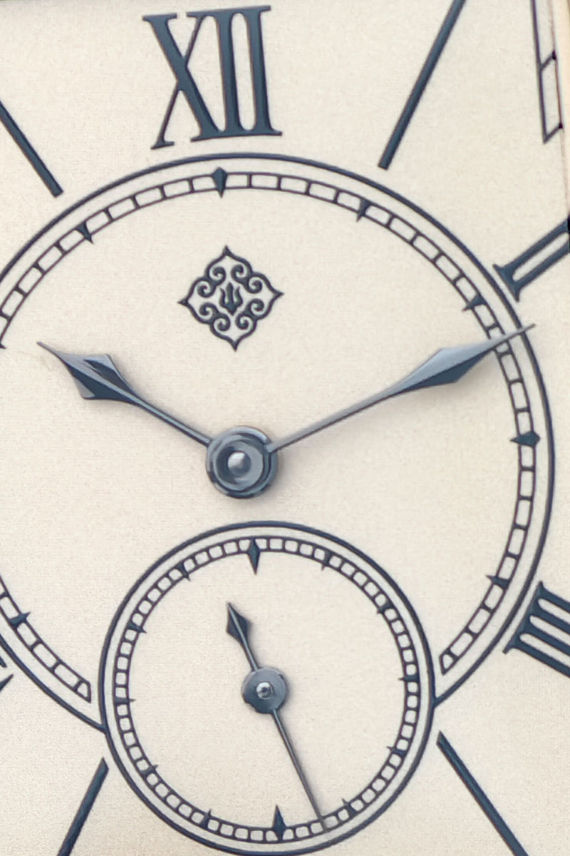 Close-up of a vintage-style clock face with Roman numerals, dark blue hands, and a small subdial on an off-white background.