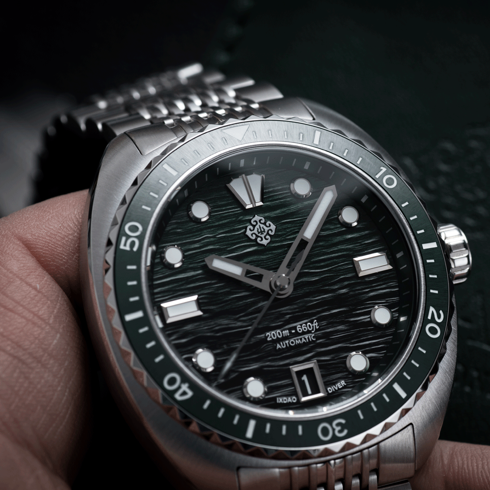 A close-up of a wristwatch being held in a hand, featuring a silver stainless steel case, a dark green bezel, and a textured dark green dial with luminous hour markers and a date window.