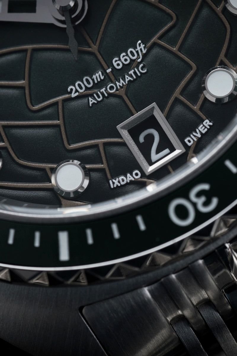 Close-up of a black automatic dive watch dial with textured geometric markings, a date window, and a black metal bracelet.
