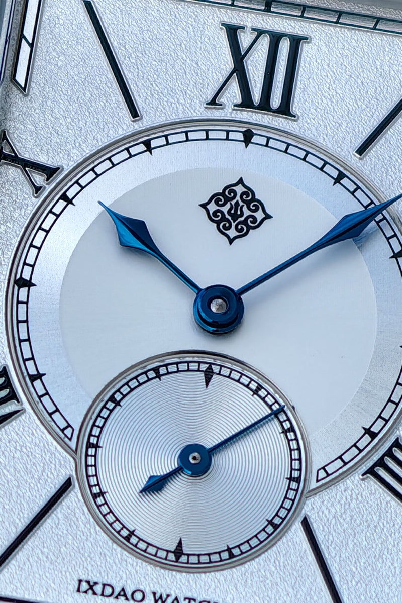 Close-up of a white dial watch face with black Roman numerals, blue hands, and a small subdial, branded IXDAO WATCH.
