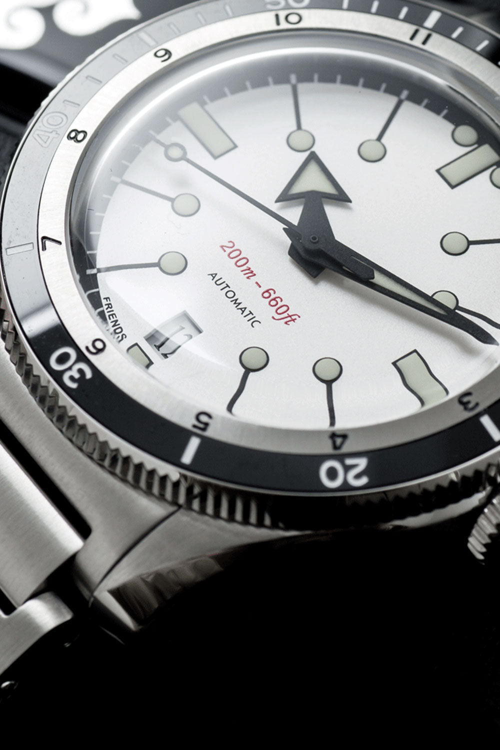 Close-up of a stainless steel wristwatch with a white dial, black bezel, and silver-tone metal bracelet against a dark background.