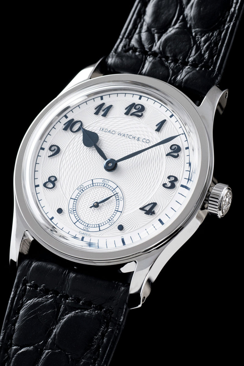 A close-up of a Headac Watch Co. wristwatch featuring a silver-toned oval case, a white dial with black Arabic numerals and hands, and a textured black leather strap with an alligator pattern, set against a solid black background.